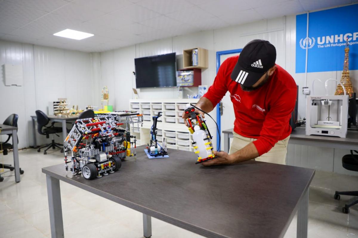 مدرب الروبوتكس في مخيم الزعتري مروان الزعبي يحمل الانسان الآلي لتعقيم اليدين (عمان نت)