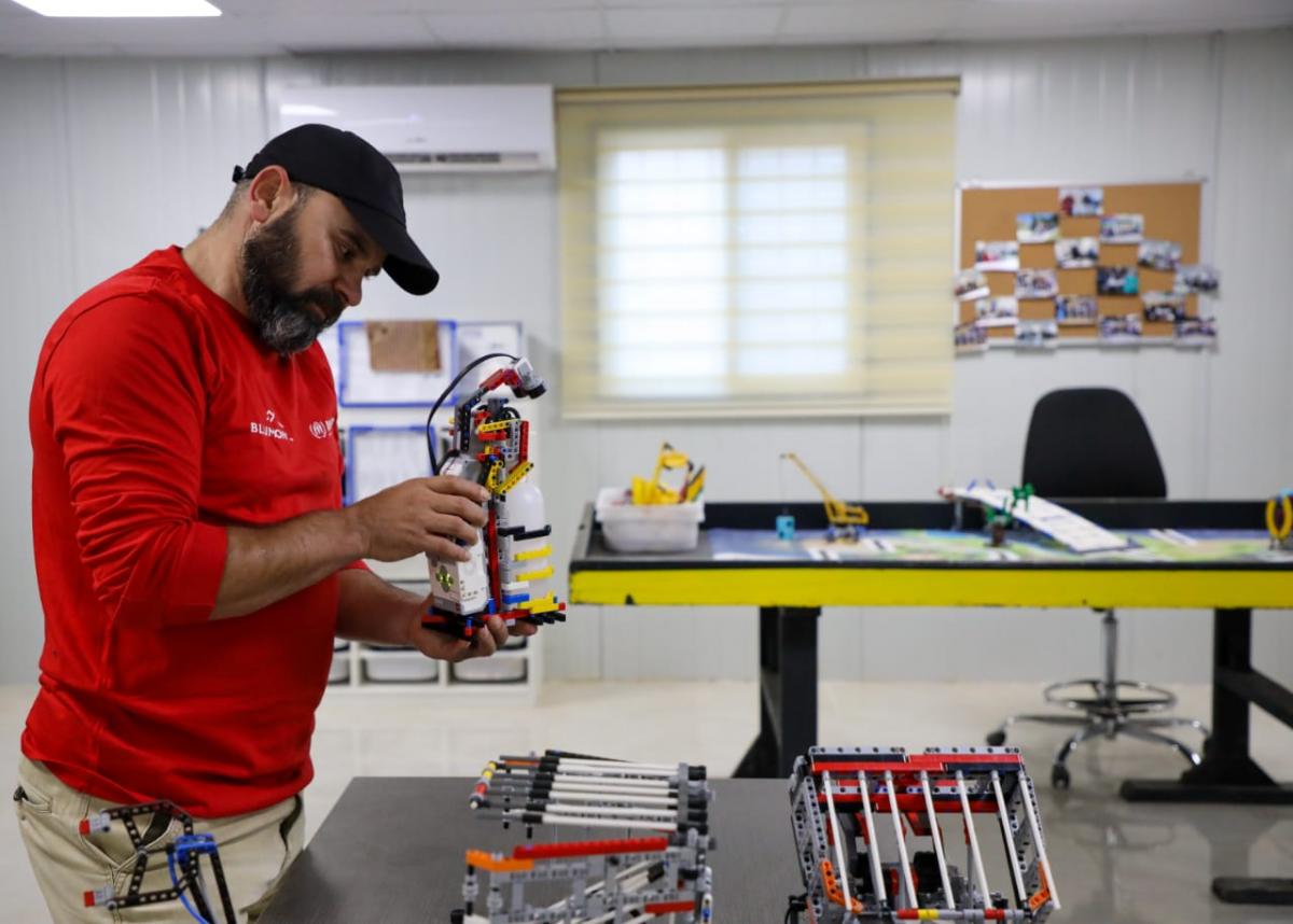 مدرب الروبوتكس في مخيم الزعتري مروان الزعبي يحمل الانسان الآلي لتعقيم اليدين (عمان نت)